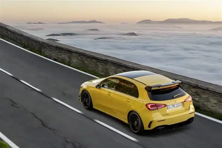 an image of a yellow AMG A35 Hatchback moving along the side of a sea on a road