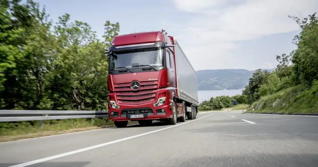 an image showing a red colour long distance truck on the road