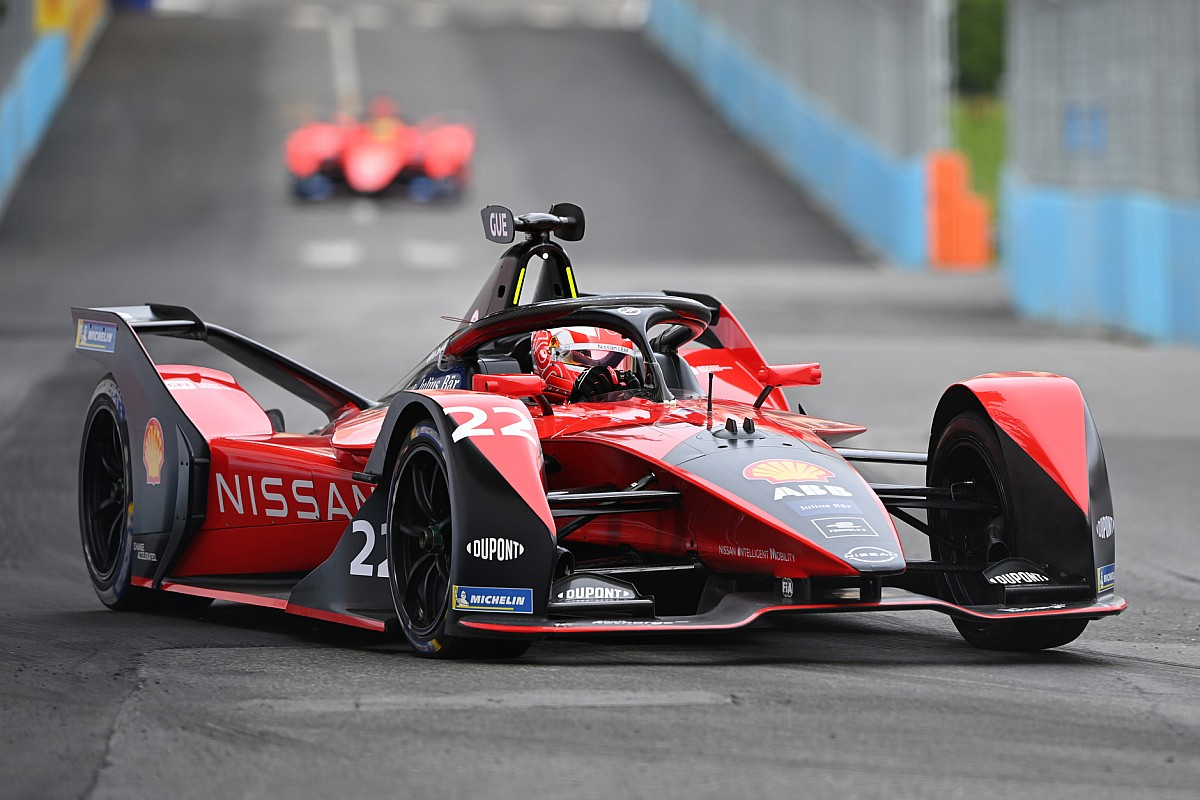 A close-up of a red and black Nissan Formula E race car speeding on an asphalt track during a competition.
