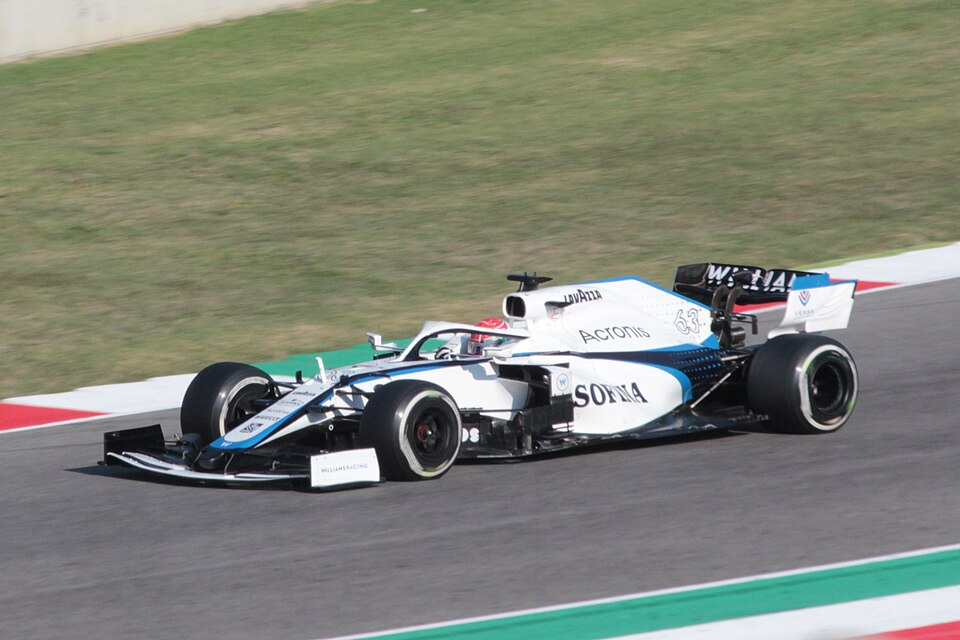 A white and blue Formula 1 race car speeding along a circuit track with grass in the background