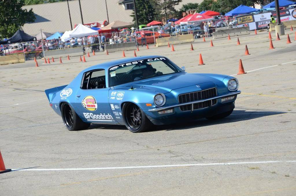A blue vintage muscle car drifting on an asphalt autocross course marked with orange traffic cones