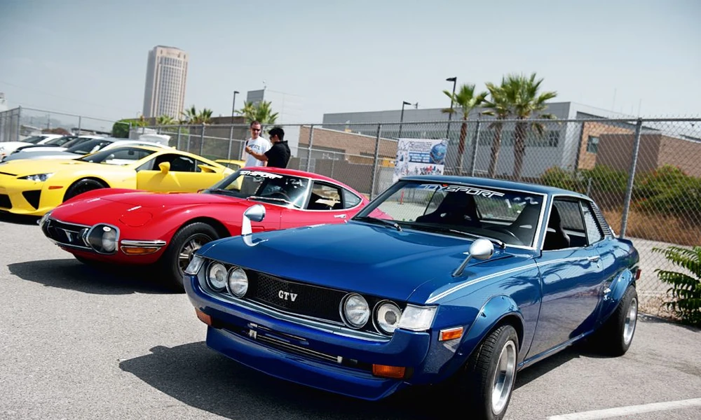 Blue classic Toyota Celica GT, with a red sports car and a yellow car behind it, at a car meet