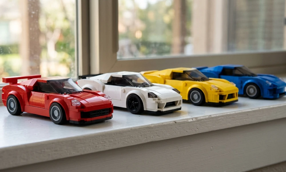 Four small LEGO Speed Champions cars in red, white, yellow, and blue on a windowsill