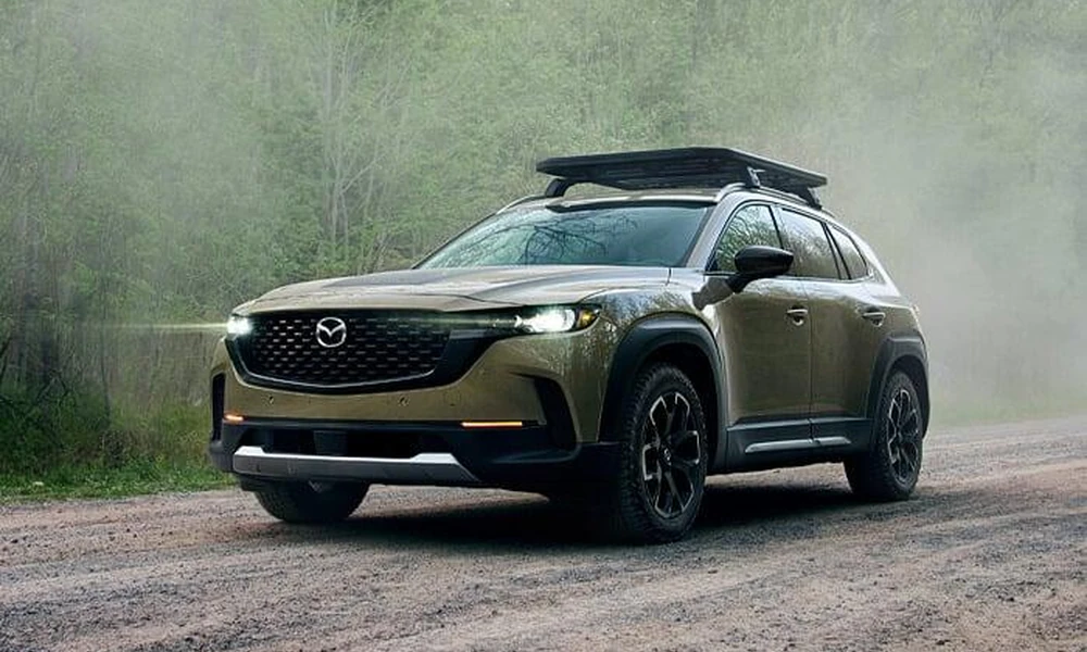 Mazda CX-50 crossover parked on a gravel road beside trees.