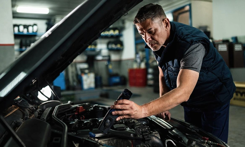 Mechanic inspecting a used car engine in a repair workshop.