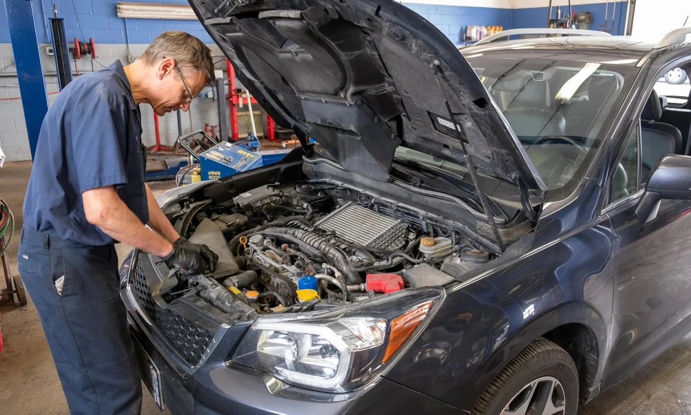 Mechanic inspecting the engine of a used car with its hood open.