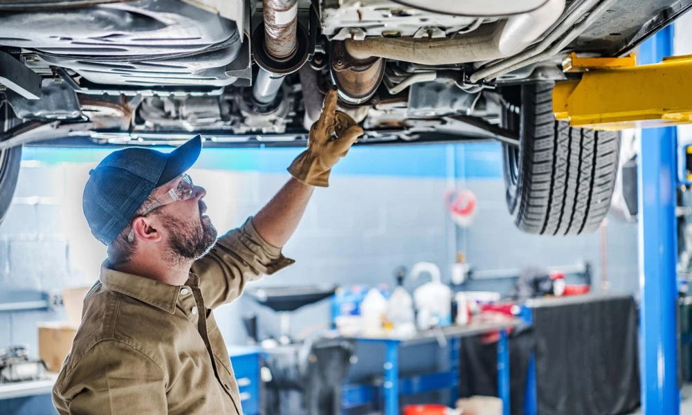 Mechanic inspecting the underside of a used car on a vehicle lift.
