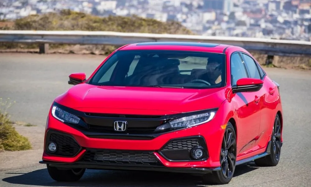 Red Honda Civic hatchback driving on a road with a city view behind it