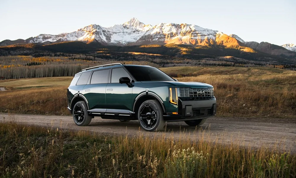 Green Kia Telluride on a dirt road with snowy mountains in the distance