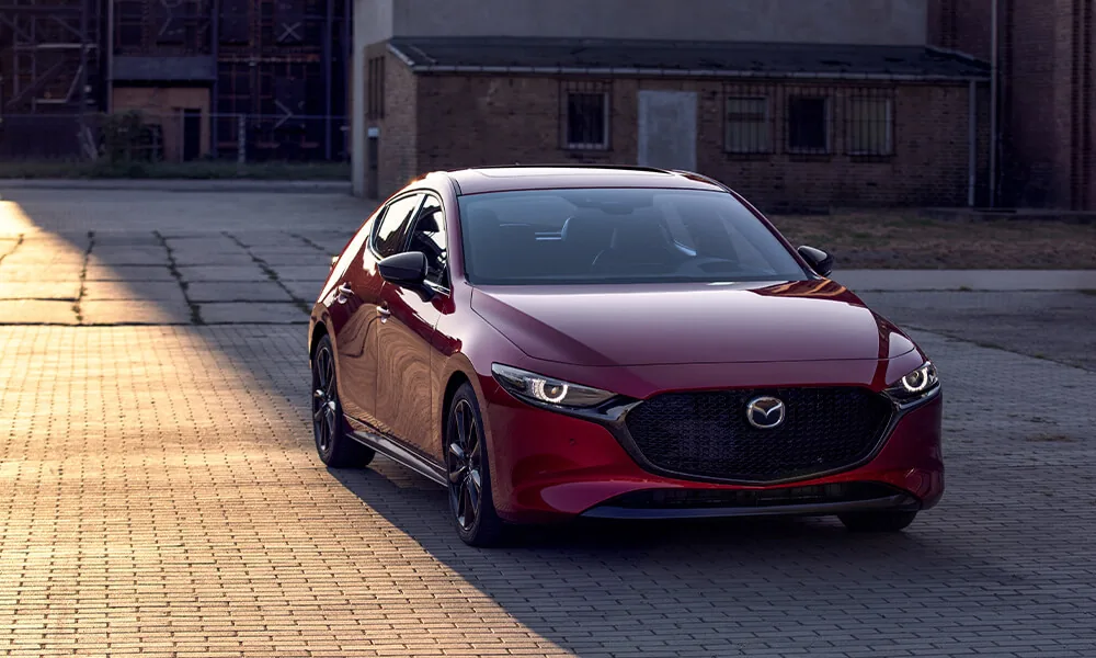 Red Mazda3 hatchback parked on a brick-paved square at sunset