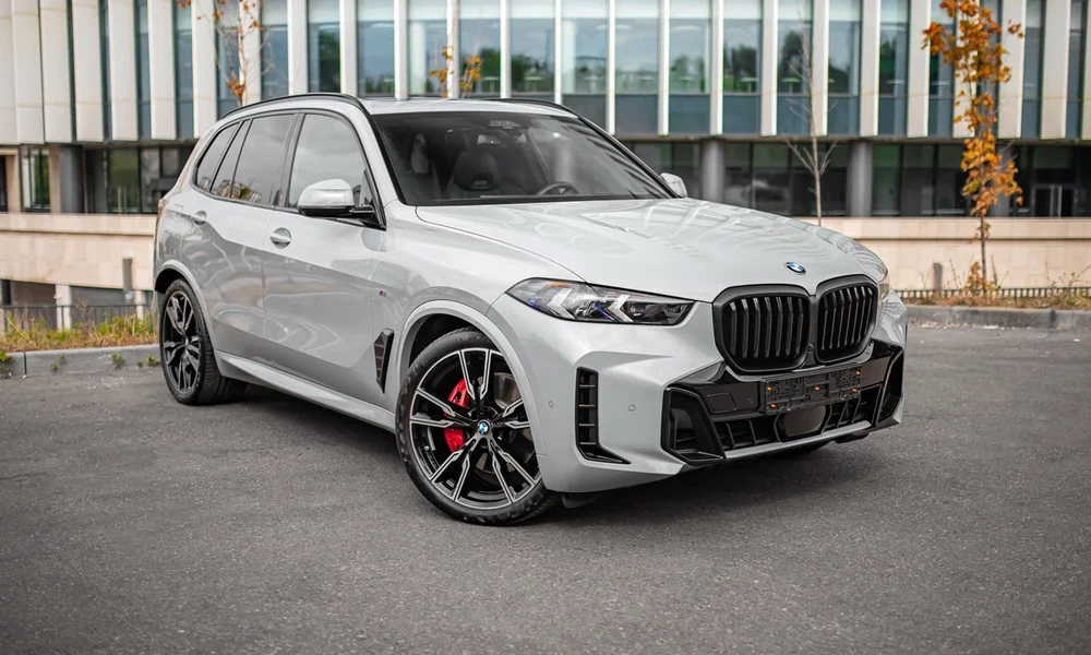 Silver BMW X5 with red brake calipers parked outside a glass office building
