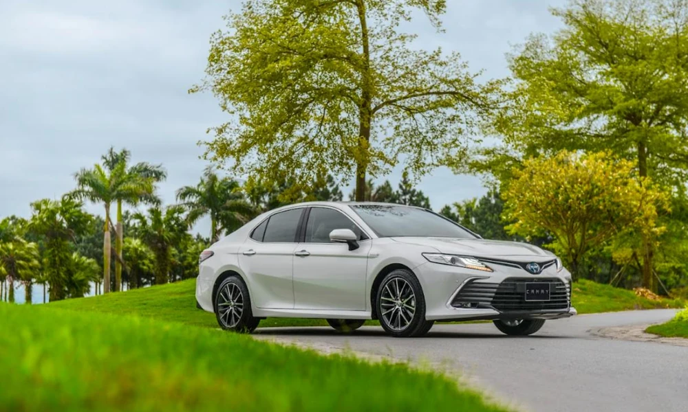 Modern hybrid sedan parked in a green landscaped area.