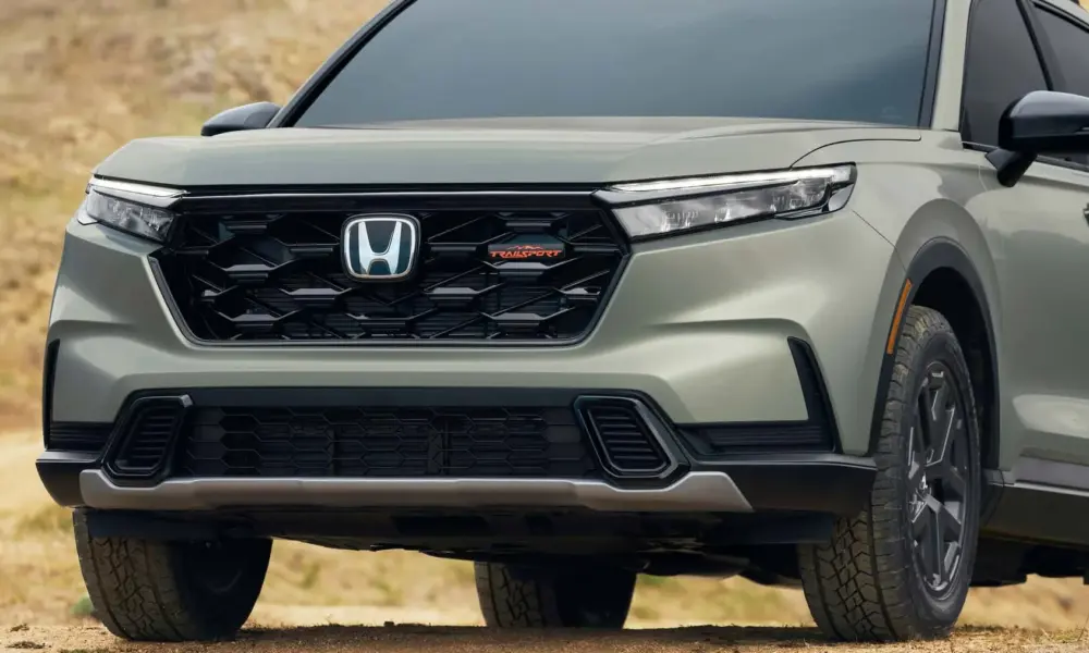 A close-up shot of the front grille of a modern sage green Honda CR-V