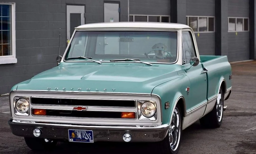 Turquoise Chevrolet C10 pickup truck with a white roof, chrome grille, and classic styling, photographed outside a building.