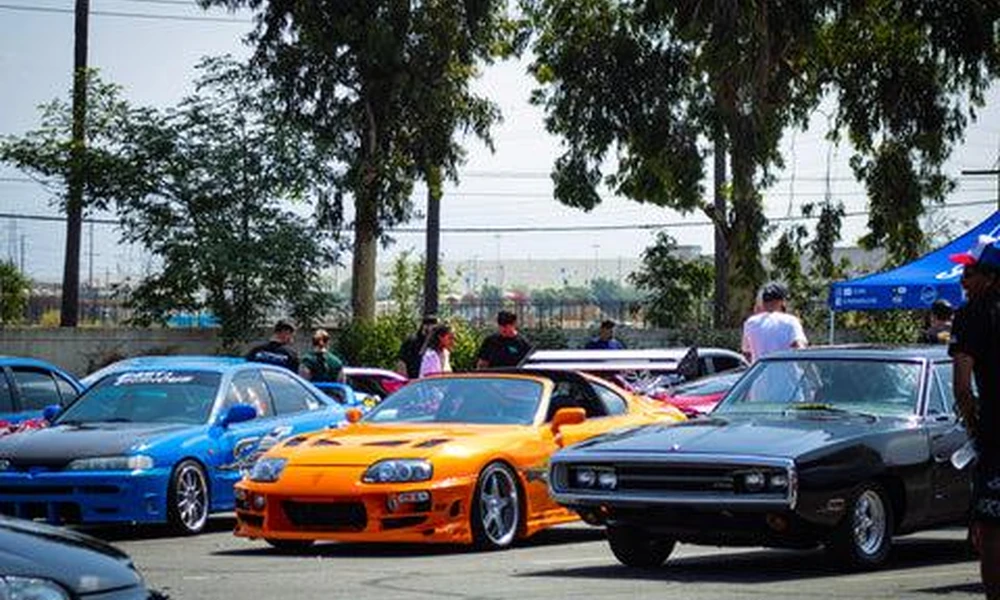 Japanese tuner sports cars and American muscle cars displayed at an outdoor car meet.