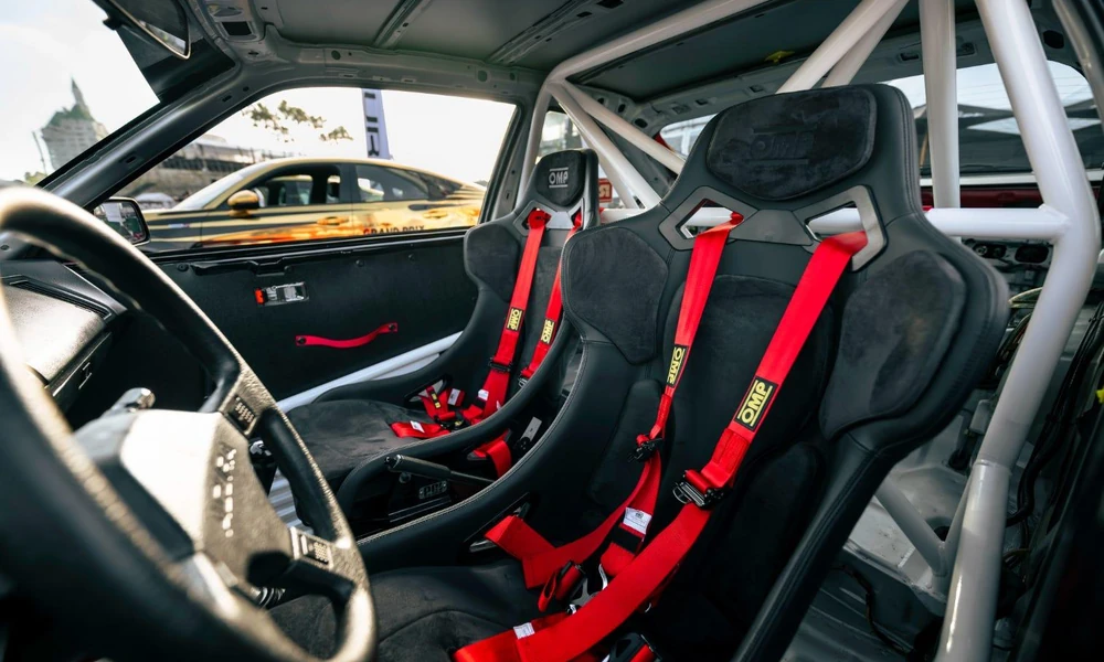 Motorsport car interior with a racing seat, safety harness, and roll cage.