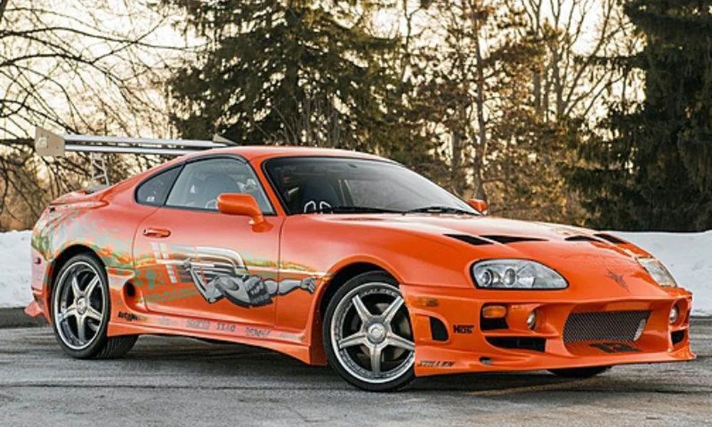 Orange modified Toyota Supra with racing graphics and a rear spoiler.