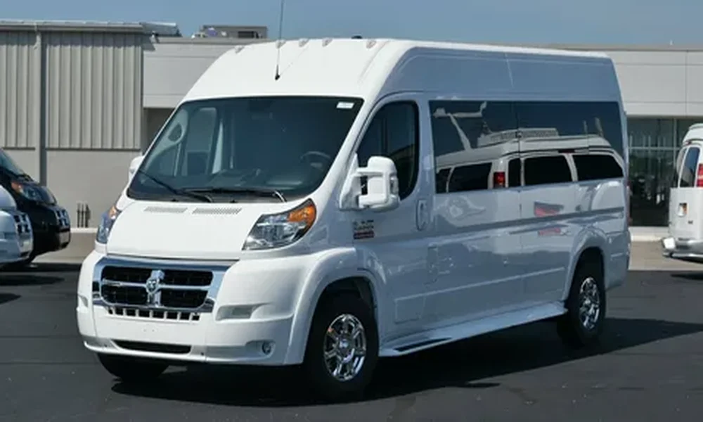White high-roof conversion van with tinted rear windows and chrome wheels, parked in a lot in front of a building.