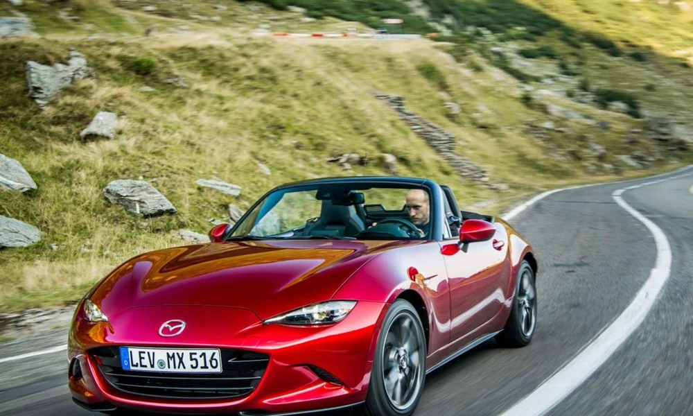 Red Mazda MX-5 Miata roadster parked with its roof down in front of a hillside