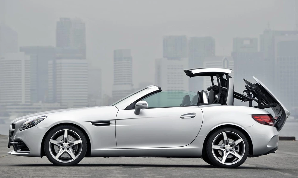 Silver Mercedes-Benz SLC with its retractable hardtop folding back, city skyline in the haze behind