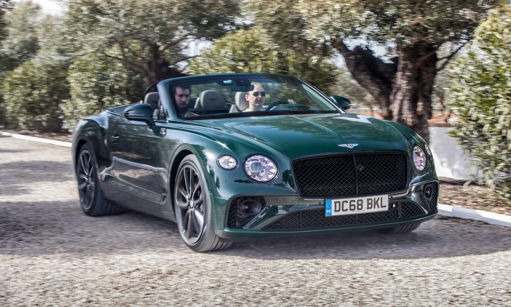 Green Bentley Continental GTC convertible with the roof down driving past olive trees