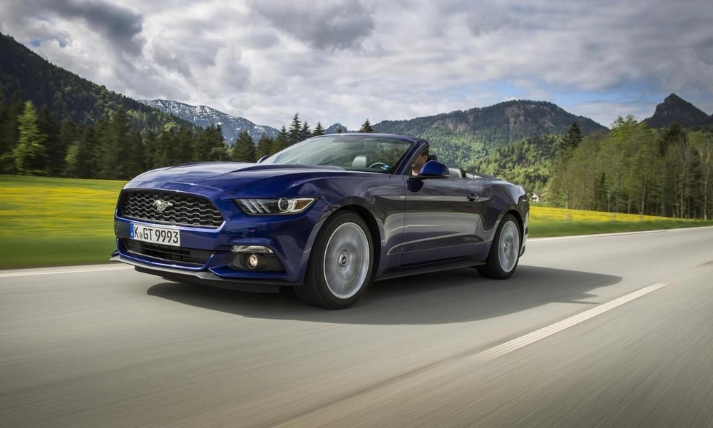 Blue Ford Mustang Convertible driving on a mountain road beside a green meadow