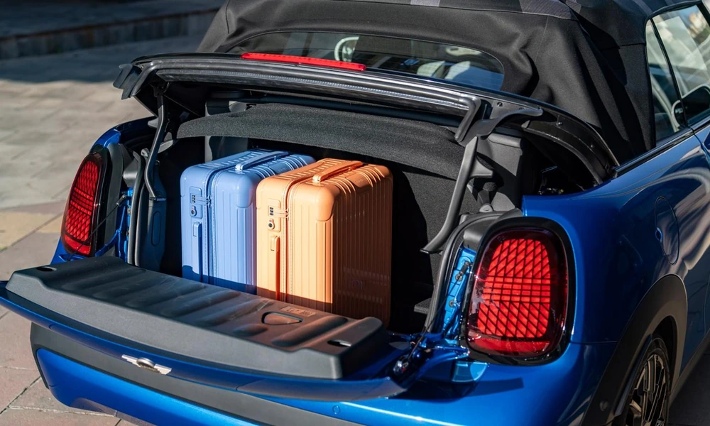 Open trunk of a blue Mini Convertible holding two small suitcases with the soft top raised