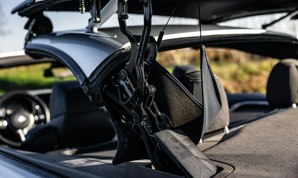 Close-up of a convertible’s folding roof mechanism showing hinges, springs, and linkages
