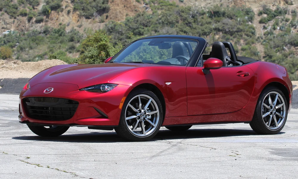 Red Mazda MX-5 Miata roadster with the roof down driving along a winding mountain road