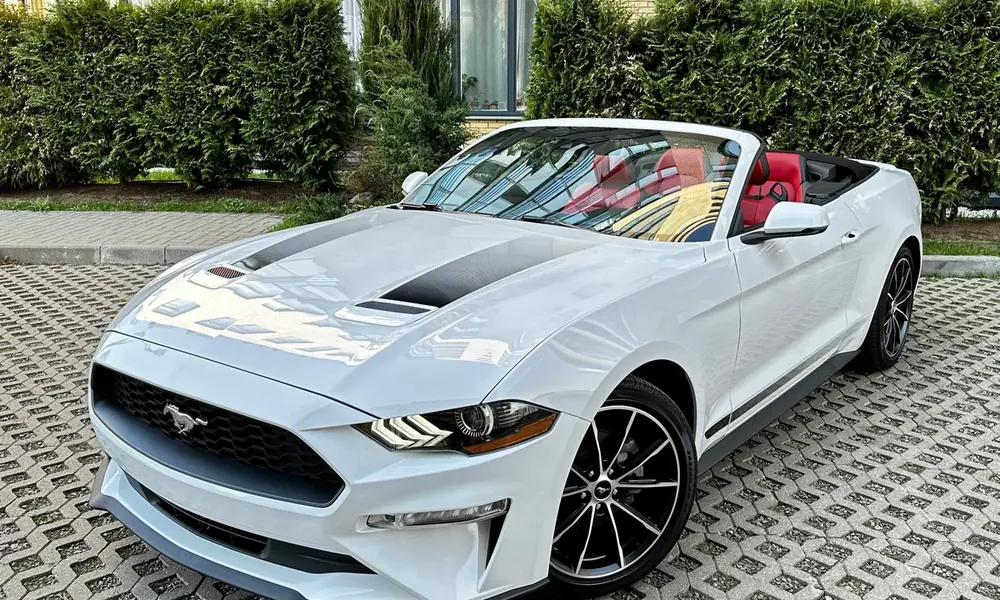 White Ford Mustang Convertible with red leather seats and the roof down, parked outside an apartment building