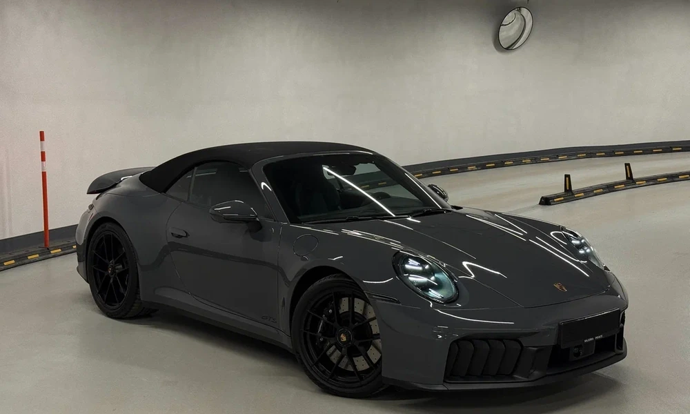 Dark grey Porsche 911 Cabriolet with a black fabric roof raised, parked in an underground garage