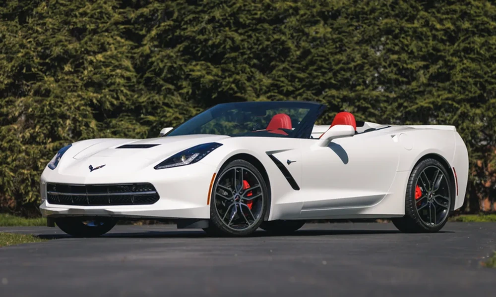 White Chevrolet Corvette Convertible with red seats and the roof down, parked in front of tall hedges