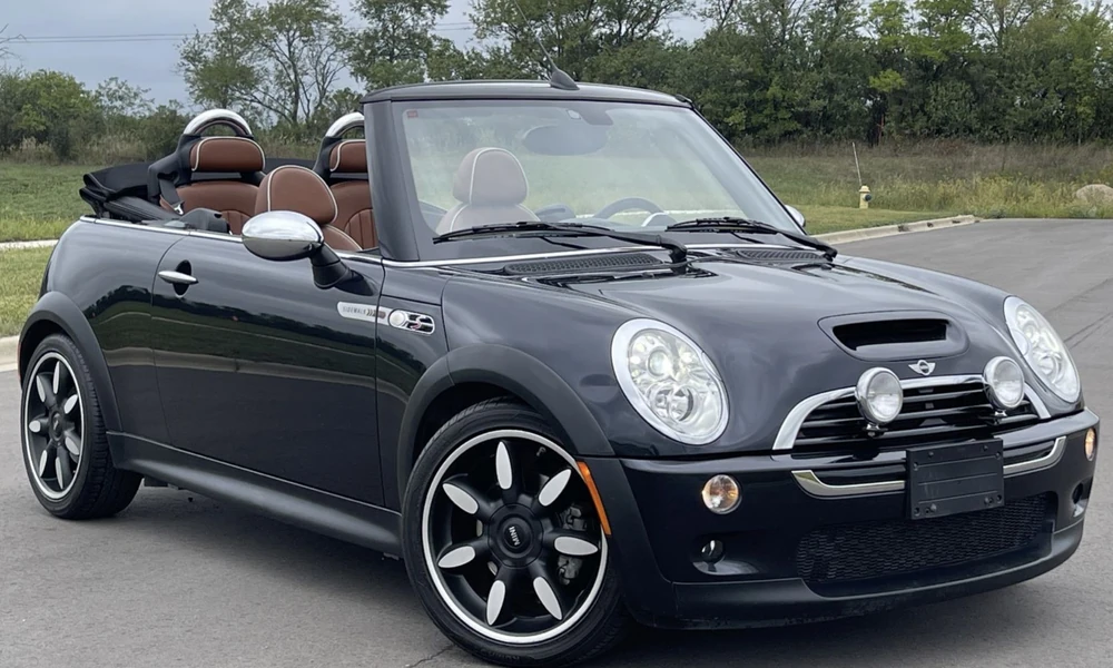Black Mini Cooper Convertible with brown leather seats and the roof folded down, parked on an empty road