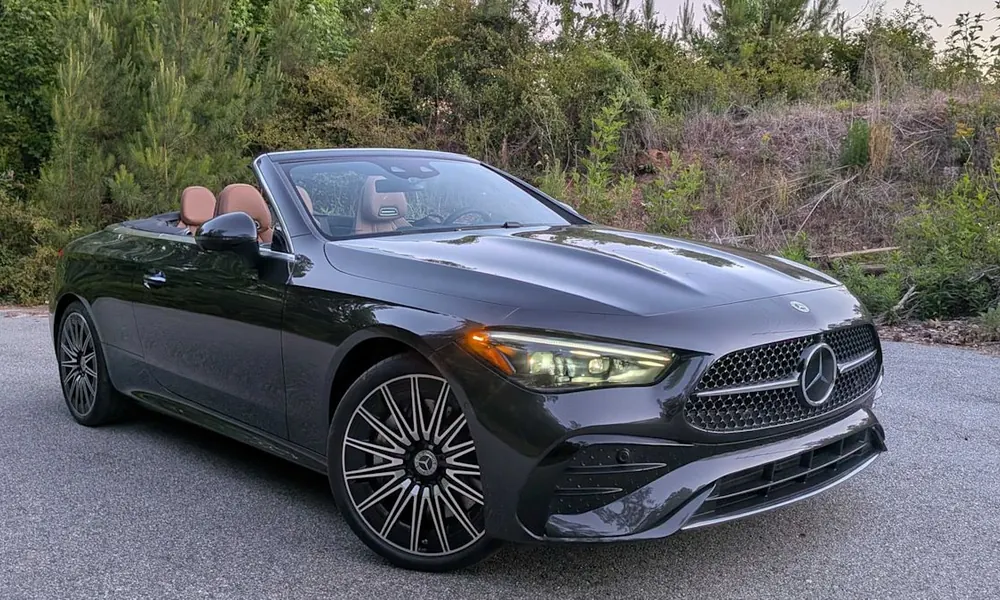Dark grey Mercedes-Benz CLE Cabriolet with tan leather seats and the roof down, parked near greenery