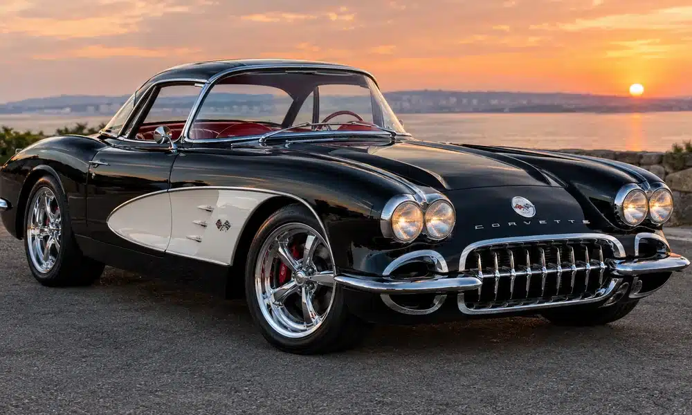 Black and white 1950s Chevrolet Corvette C1 with chrome grille and dual headlights parked by the sea at sunset