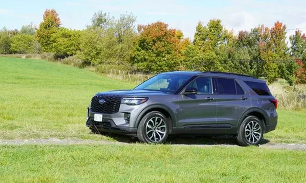 Gray Ford Explorer parked on a grass trail with trees in autumn colors behind it