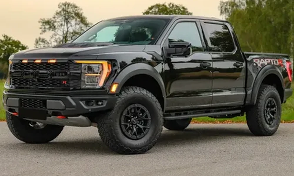 Black Ford F-150 Raptor pickup with large off-road tires and an orange light bar in the grille