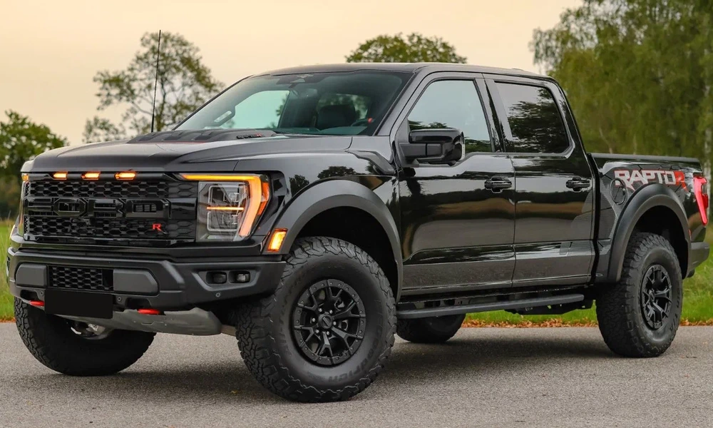 Black Ford F-150 Raptor parked on pavement with trees behind it