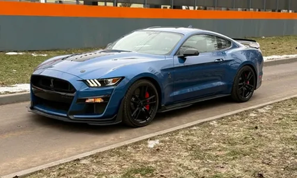 Blue Ford Mustang with black wheels and red brake calipers parked on a road beside a grass verge