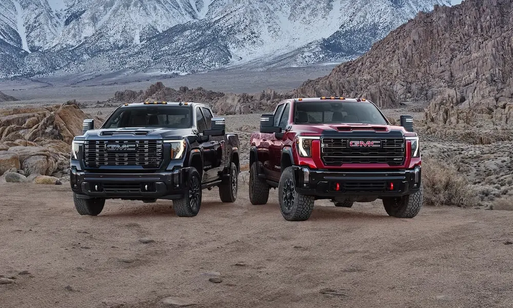 Black and red GMC Sierra pickups parked side by side on desert ground with snowy mountains behind