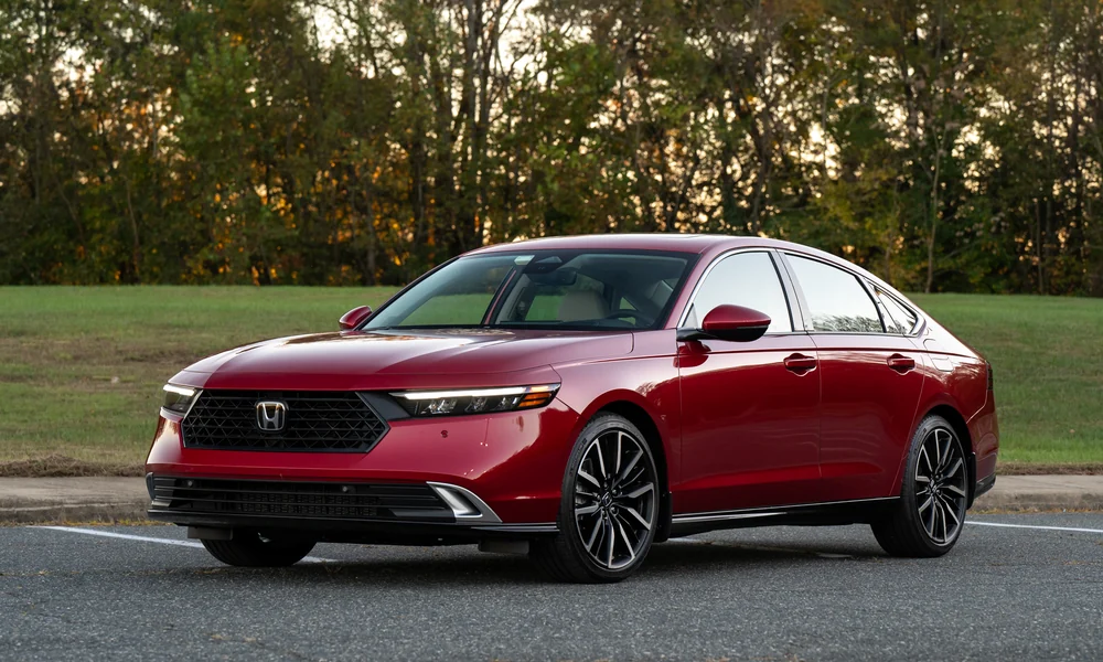 Red Honda Accord Hybrid sedan parked on a road with trees behind it