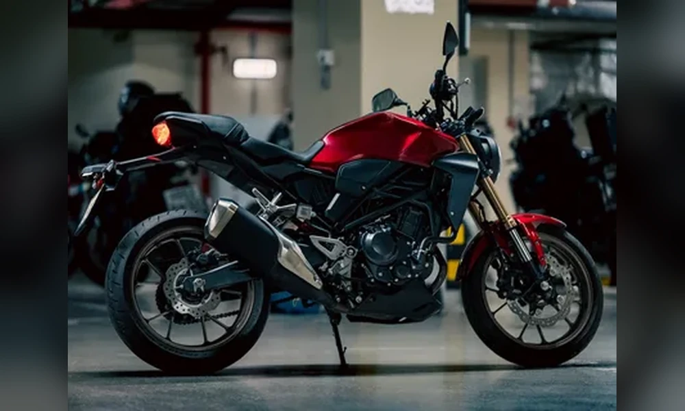 Red Honda CB300R naked motorcycle with gold front forks and black exhaust, parked in an underground garage, side view