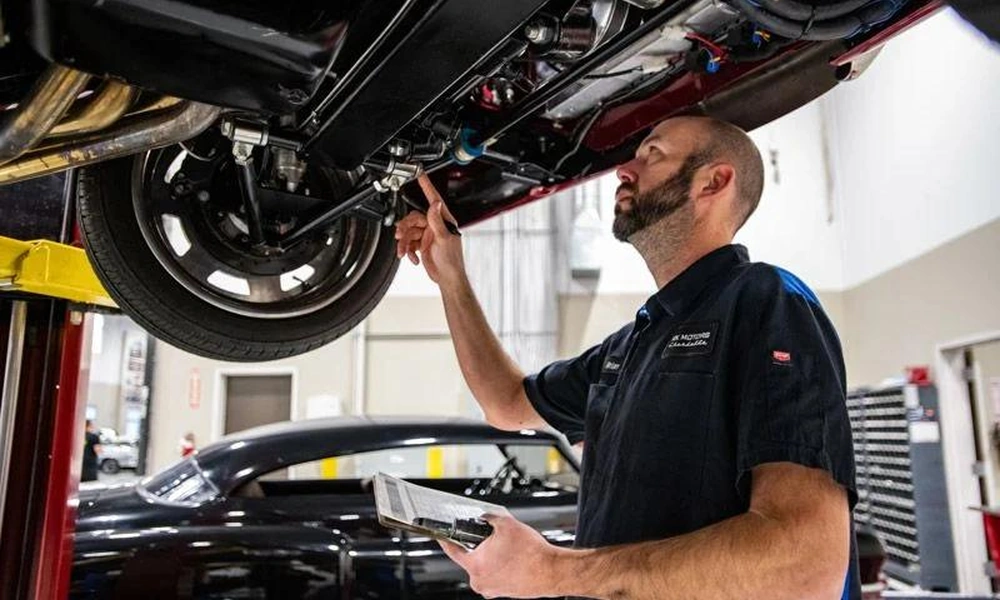 Mechanic inspecting the underside and chassis of a vintage car in a workshop.