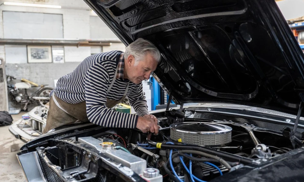 Mechanic restoring a vintage American car in an automotive workshop.