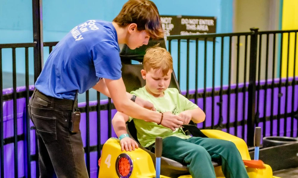Amusement park operator helping a child secure a bumper car seat belt.