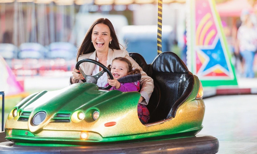 Parent and young child enjoying a two-seater bumper car ride at an amusement park.