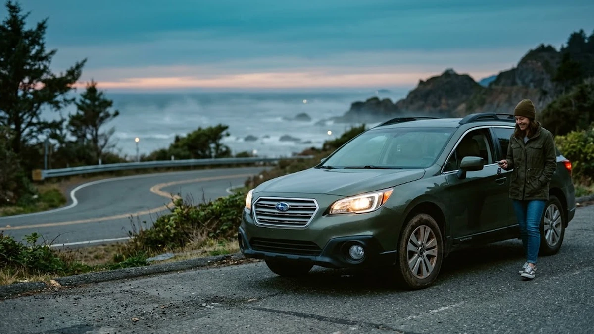 Buyer holding a car key beside a used green SUV on a coastal road at dusk