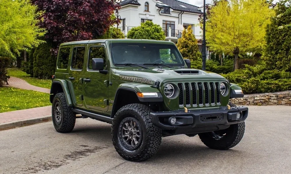 Green Jeep Wrangler Rubicon with off-road tires parked on a paved street