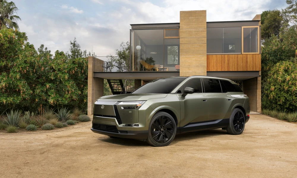 Green Lexus TZ electric SUV parked on sandy ground in front of a modern house