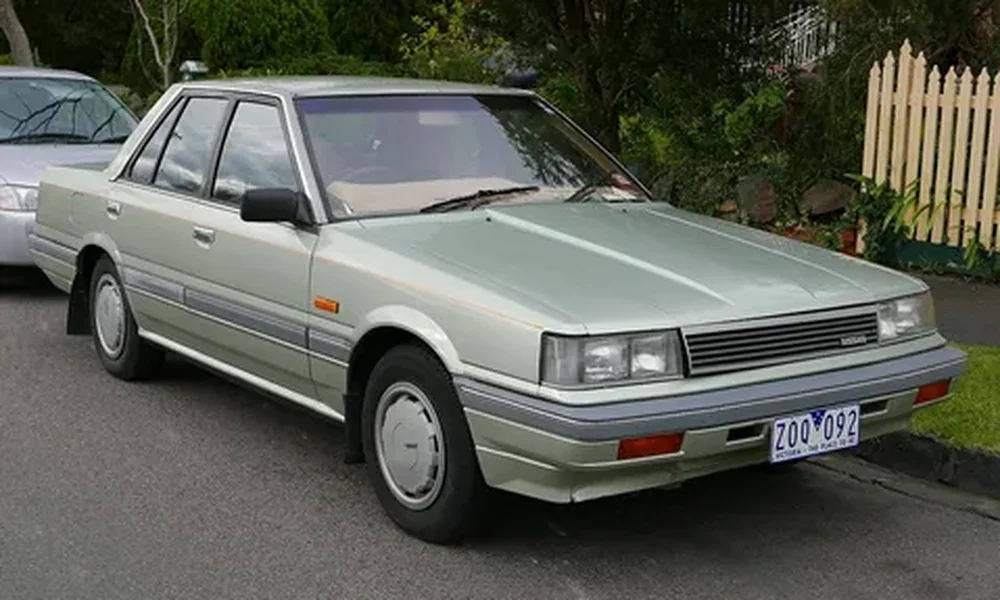 Light green Nissan Skyline R31 four-door sedan with rectangular headlights and silver wheel covers, parked on a residential street.